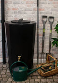 Midi Metro 185L Water Butt - Black Slim Cylindrical Tank next to gardening tools and a watering can.