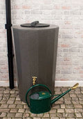 Millstone Midi Metro 185L Water Butt - Millstone Effect next to a green watering can on cobblestone