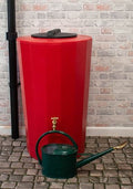 Midi Metro 185 Litre Water Butt - Red Slim Cylindrical Tank beside green watering can on cobblestone flooring.