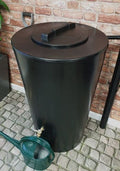 City Just Water 210L Water Butt - Black Slimline Garden Tank placed beside a watering can on a paved patio.