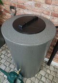 City Just Water 210L Millstone Effect Water Butt - Slimline on cobblestone patio with garden tools.