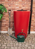 City Just Water 210 Litre Water Butt - Red Slimline Design next to gardening tools on cobblestone floor.