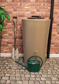 City Just Water 210L Water Butt - Sandstone Effect Slim Design next to gardening tools on cobblestone patio.