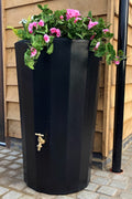 Black Midi Metropolitan Water Butt Planter - 165L Black with flowers on top near outdoor wooden wall