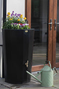 Black Midi Metropolitan Water Butt Planter - 165L Black with colorful flowers and a green watering can.