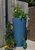 Blue Marble Metropolitan Water Butt Planter - 255L Blue Stone Effect with plants against wooden fence.