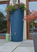 Bluestone Big City Water Butt Planter - 380L Blue Stone-Effect with colorful flowers on top near patio.