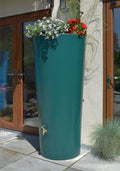 Green Big City Water Butt Planter - 380L Capacity with flowers on top placed near a building entrance.