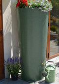 Big City Water Butt Planter - Green Marble 380L with flowers, beside watering can and potted plants.