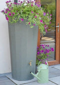 Metropolitan 255L Water Butt Planter - Green Marble Effect with flowers and watering can near a door.