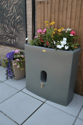 Green Marble Oasis 375L Water Butt Planter - Cylindrical 120cm with flowers on top against a wooden fence