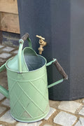 Millstone Midi Metropolitan Water Butt Planter - 165L Stone Effect beside a green watering can and spigot.
