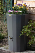Millstone Midi Metropolitan Water Butt Planter - 165L Stone Effect with flowers and plants in a garden setting.