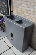 Millstone Oasis 375 Litre Water Butt Planter - Millstone Effect against a brick wall with flowers.