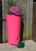 Pink Metropolitan 255L Water Butt Planter - Decorative Pink with flowers and watering can beside it.