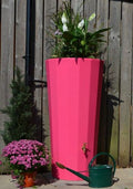 Pink Metropolitan 255L Water Butt Planter - Decorative Pink with flowering plants and watering can beside.
