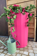 Midi Metropolitan 165L Water Butt Planter - Pink with flowers and a green watering can in a garden setting.
