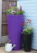 Metropolitan 255L Water Butt Planter - Purple Decorative Storage with flowers in a garden setting.