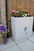 Oasis 375L Water Butt Planter - White Marble Effect with colorful flowers in a modern outdoor setting.